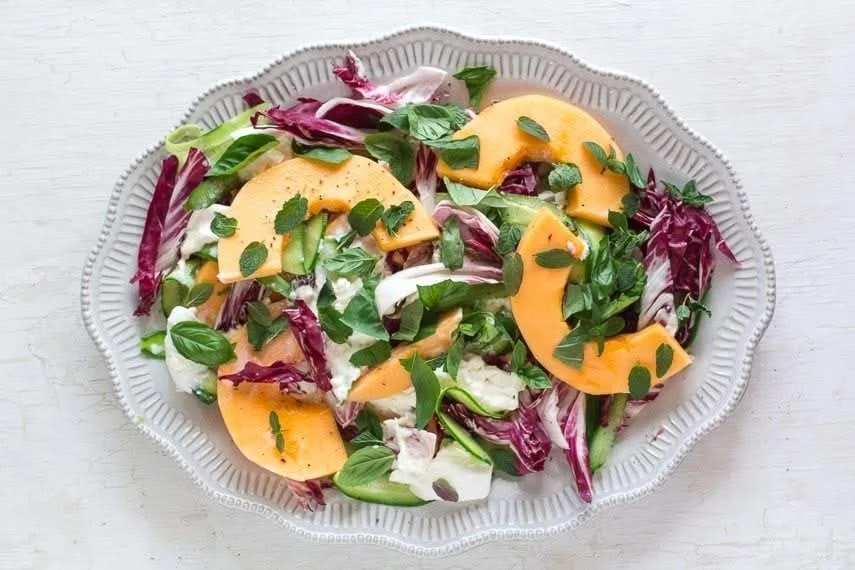 Low FODMAP cantaloupe salad with cucumber and burrata cheese garnished with herbs.