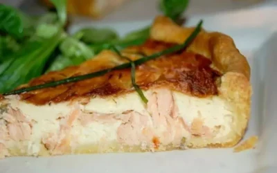 Quiche al salmone appena sfornata su un piatto bianco decorato con erbe fresche