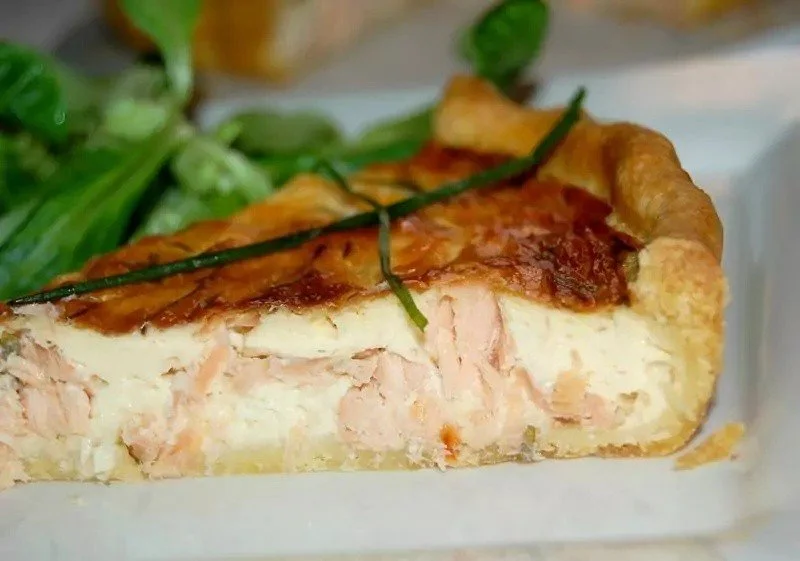 Quiche al salmone appena sfornata su un piatto bianco decorato con erbe fresche
